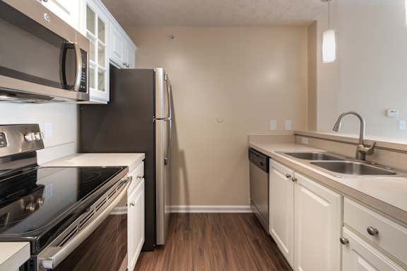 Galley kitchen in the Catamaran 1-bedroom apartment at Nantucket Apartments in Loveland, Ohio, with white cabinetry, stainless-style appliances, double sink, and wood-style flooring.