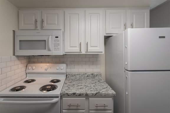 A kitchen with a white cabinets 1 bedroom, 1 bath apartment home and white appliances at Princeton Court Apartments in the Vickery Midtown neighborhood of Dallas, TX.
