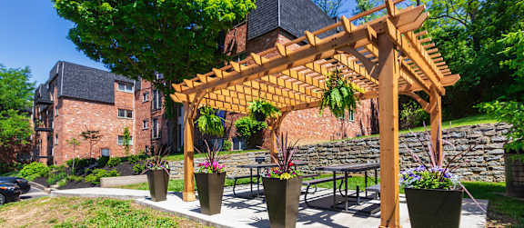 A wooden pergola with hanging plants is in front of a apartment buildings at Romaine Court Apartments in the Oakley neighborhood of Cincinnati, Ohio.