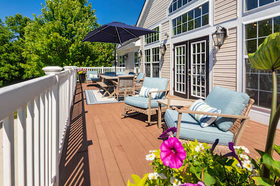 A patio with a white railing, a blue cushioned chair, and a white building with windows.