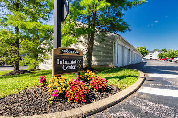 A sign for the Sauder Lumber Information Center is surrounded by flowers and trees.