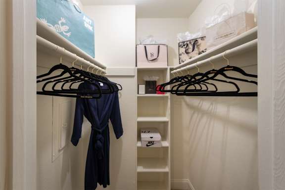 Bedroom walk-in closet with a blue robe hanging  and built-in shelving in the 558 square foot 1 bedroom, 1 bath model apartment at The Summit at Midtown Apartments in the Dallas Midtown neighborhood of Dallas, TX.