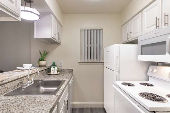 alley kitchen with white cabinets, granite-style countertops, electric range, and refrigerator in a 558-square-foot one-bedroom apartment