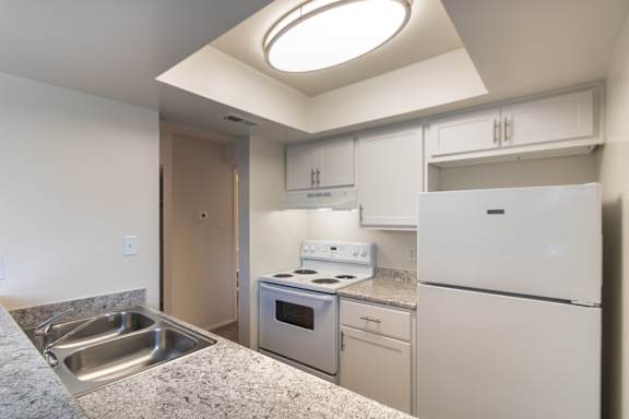 Kitchen view in the 684 sq. ft. 1-bedroom apartment at Village East, with a double sink, electric range, refrigerator, and breakfast bar.