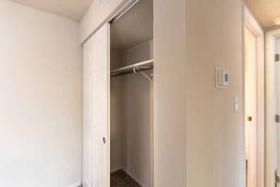 Closet and hallway view in the Village East 1-bedroom apartment, with sliding closet doors, thermostat, and bathroom access nearby.