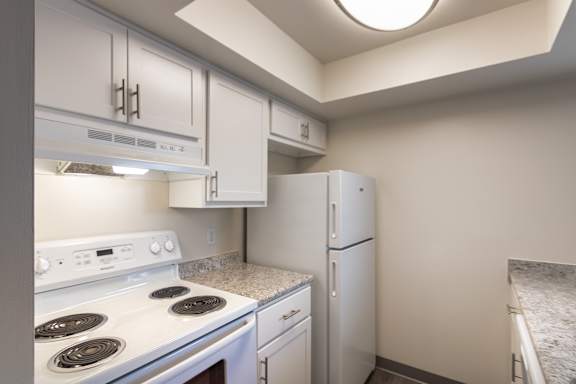 Kitchen appliance area at Village East Apartments, with an electric range, white cabinetry, refrigerator, and counter space.