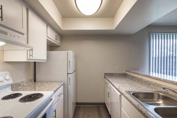 Kitchen in the Village East 1-bedroom apartment, with white cabinets, electric range, refrigerator, sink, and wood-style flooring.