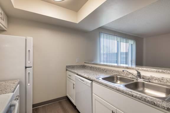 Galley kitchen at Village East Apartments, with white cabinetry, double sink, laminate counters, and refrigerator.