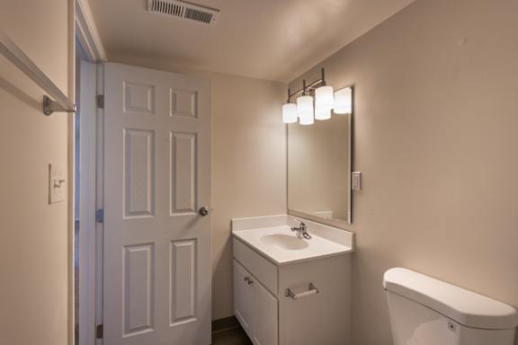 Bathroom vanity in the Village East 1-bedroom apartment, with a white sink cabinet, mirror, bright vanity lights, and toilet.