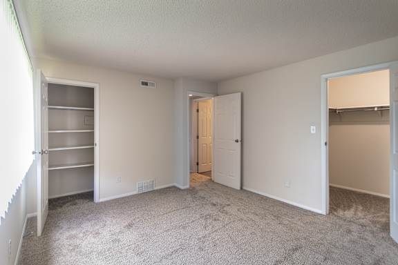 Bedroom view in the 684 sq. ft. apartment at Village East, with a window, carpeted flooring, closet shelving, and bathroom access nearby.