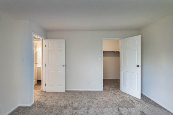 Bedroom in the Village East 1-bedroom apartment, with carpeted flooring, closet access, and the bathroom doorway visible beyond.