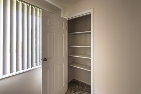 Bedroom closet at Village East Apartments in Franklin, Ohio, with built-in shelving, hanging space, and window light nearby.