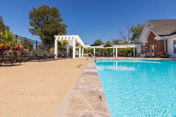 A pool with a white pergola and a house in the background.