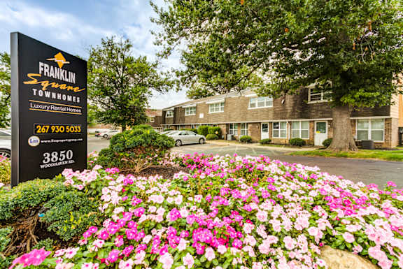 A sign for Franklin Square Townhomes is in front of a building with a flower bed in the foreground.