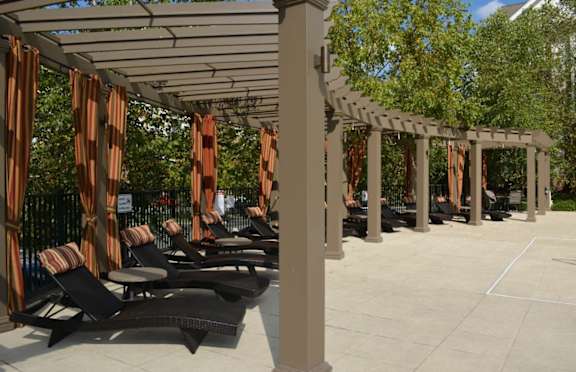 A row of black lounge chairs are arranged under a white pergola with orange curtains.at Riverview Landing @ Valley Forge, Pennsylvania
