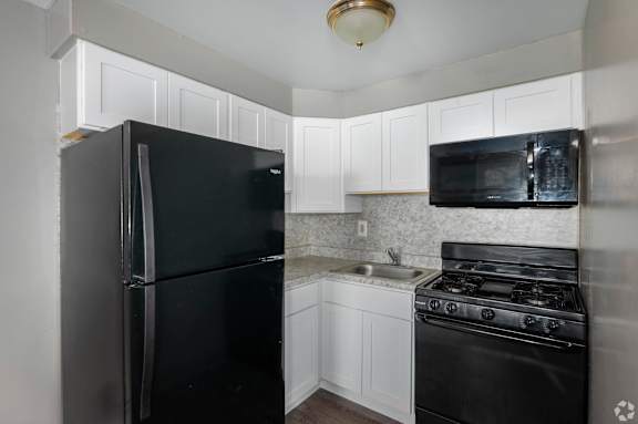 A black refrigerator and microwave in a kitchen with white cabinets.
