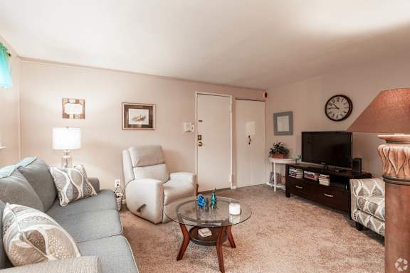 A living room with a grey couch, a white chair, a coffee table, and a television.