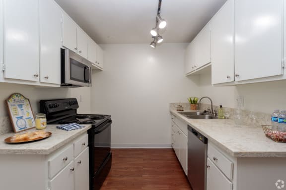 a kitchen with white cabinets and stainless steel appliances and marble counter tops at Willow Tree Apartments, Torrance, CA