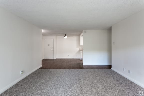 an empty living room with carpet and white walls at Willow Tree Apartments, California