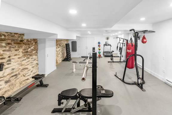 A well-equipped gym with a variety of exercise machines and a stone wall.