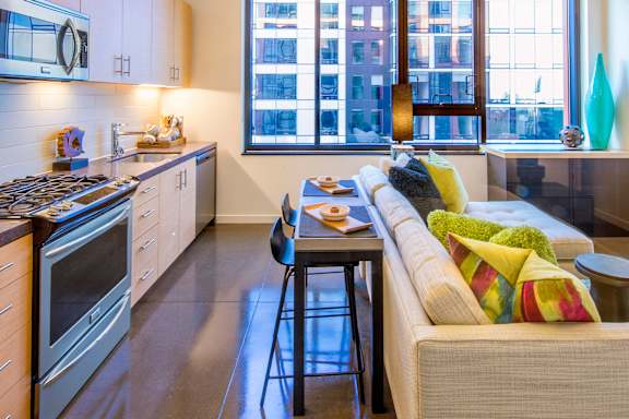 A modern kitchen with a bar stool and a couch with colorful pillows.