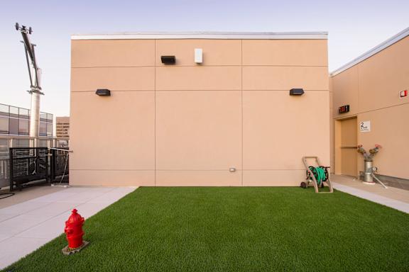 A red fire hydrant is placed on a green lawn in front of a tan building.