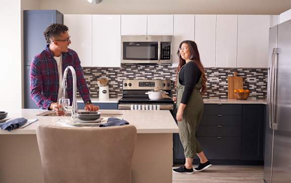 A man and woman are in a kitchen, the man is washing dishes and the woman is standing by the counter.at Linc, Des Moines Iowa