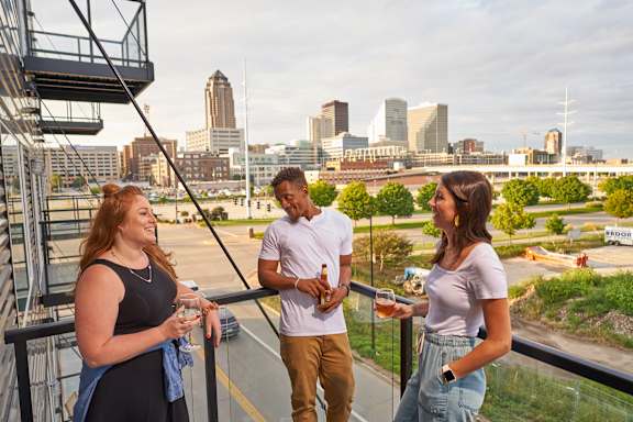 Three people are standing on a balcony with a city skyline in the background.at Linc, Des Moines, IA 50309