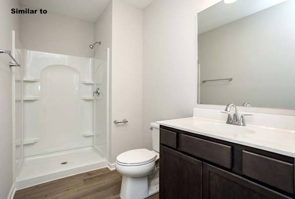 A white toilet is in a bathroom with a walk-in shower. at Two Rivers Home Rentals, West Des Moines, IA