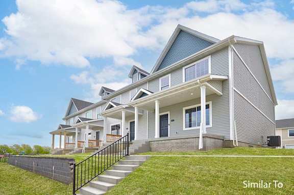 a large gray house with a porch and a green lawn at Two Rivers Home Rentals, West Des Moines