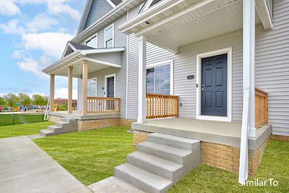 a white house with a porch and a blue door at Two Rivers Home Rentals, Iowa