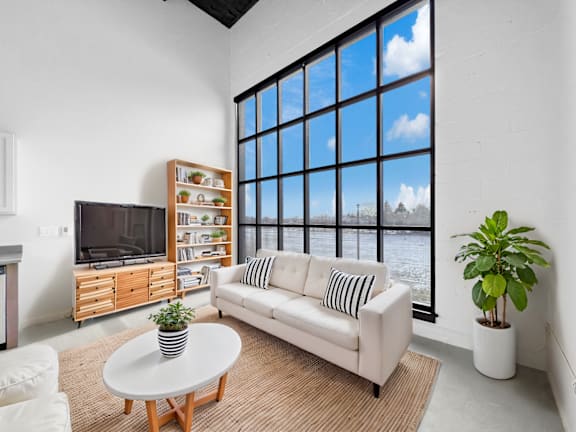 A living room with a white couch, a television, and a large window.at Plant 1 Lofts, N. Newton, 50208