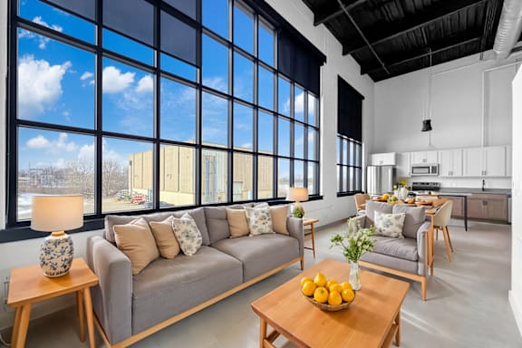 A modern living room with a grey sofa, wooden coffee table, and a large window.at Plant 1 Lofts, N. Newton, IA