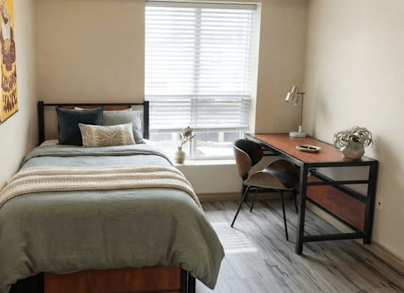 A bedroom with a bed, desk, chair, and window.