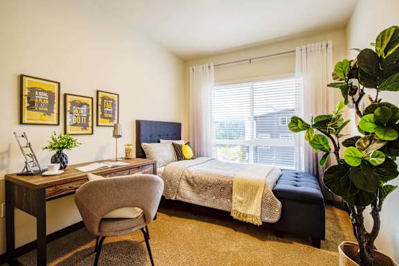 A bedroom with a bed, desk, chair, and a potted plant.
