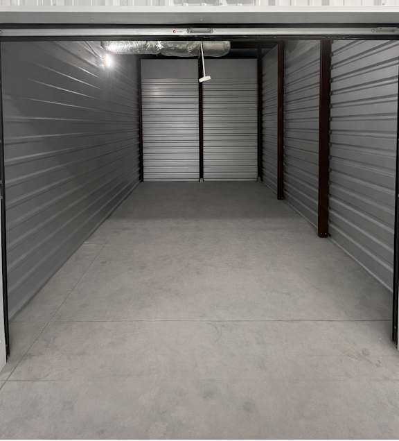 A spacious, empty storage unit with closed grey doors and a concrete floor.