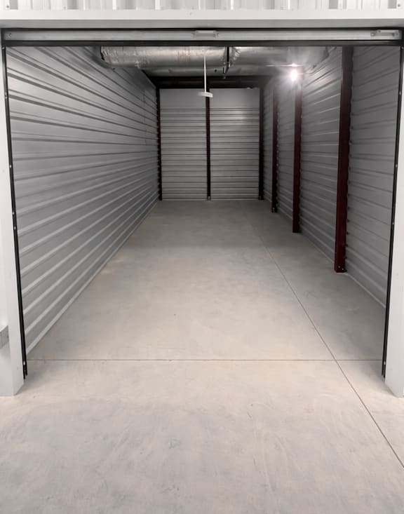 A long, narrow storage space with a concrete floor and walls covered in metal shelving.