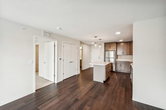 an empty living room and kitchen with wood flooring and white walls