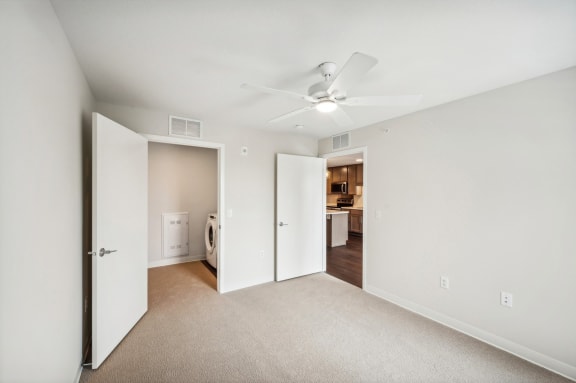 an empty bedroom with a ceiling fan and a door to a bathroom