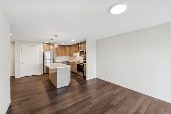 an empty living room and kitchen with wood flooring and white walls