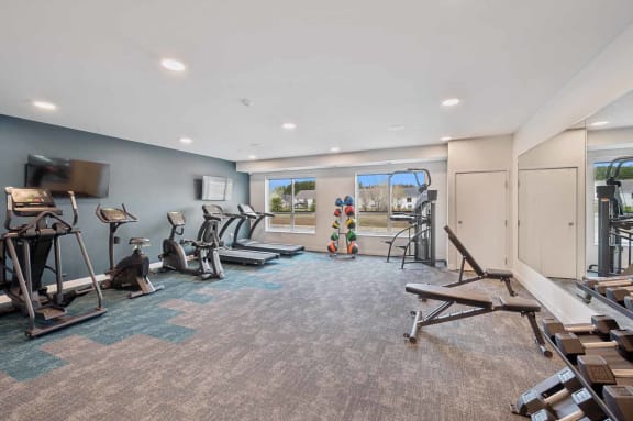 a gym with various machines and weights in a large room with windows