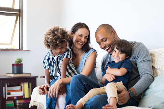 A family of four is sitting on a couch together.