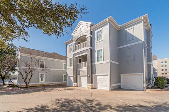 a gray apartment building with a driveway and a tree