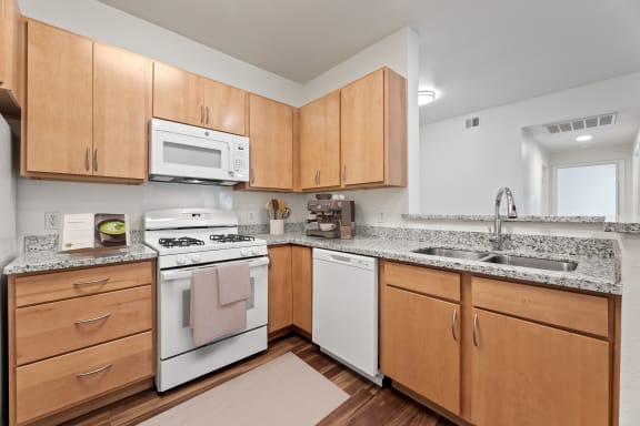 a kitchen with white appliances and granite counter tops and wooden cabinets at Sandy Creek Apartments, Bryan, Texas
