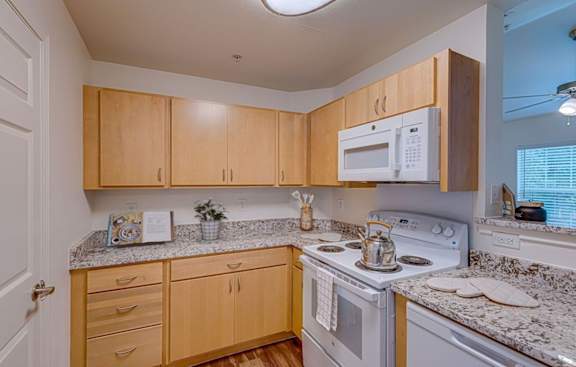 A kitchen with a white stove top oven and a white microwave above a counter with a granite counter top.