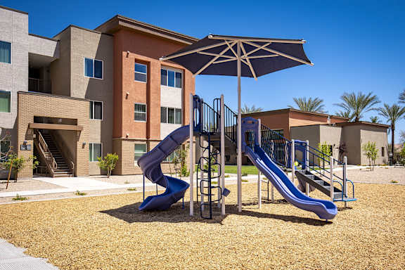 A playground with a blue slide and a brown umbrella.