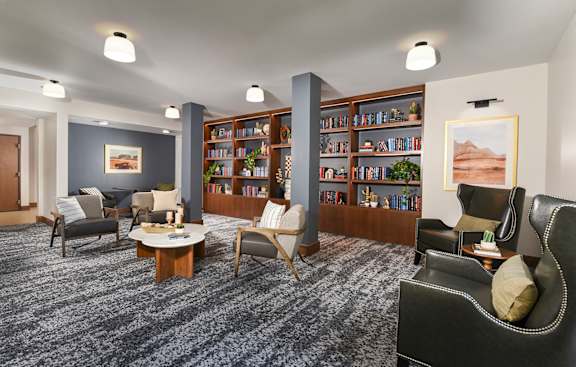 A living room with grey carpet and a bookshelf filled with books.