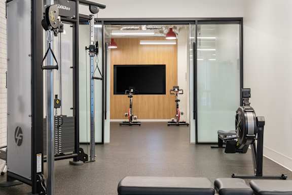 A gym with a variety of equipment including a squat rack, a bench, and a rowing machine.