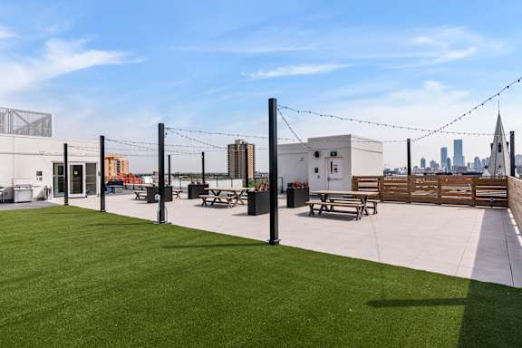 A rooftop patio with a grassy area and picnic tables.