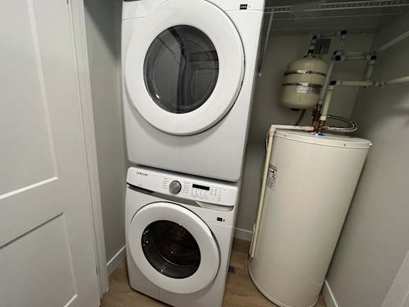 A white front load washing machine is stacked on top of a white dryer in a small laundry room.
